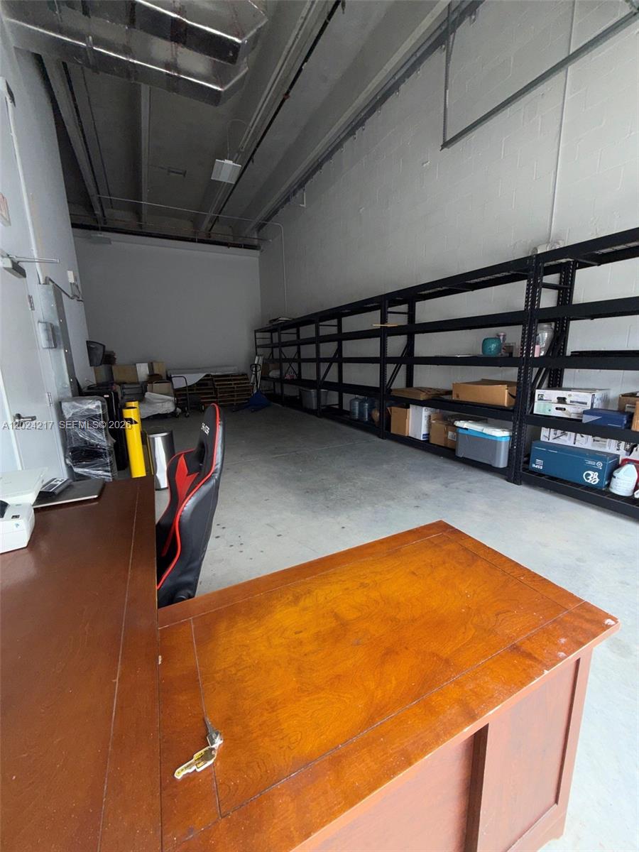 A warehouse space features a wooden desk, a gaming chair, and long metal storage shelving — SWEETWATER, FL