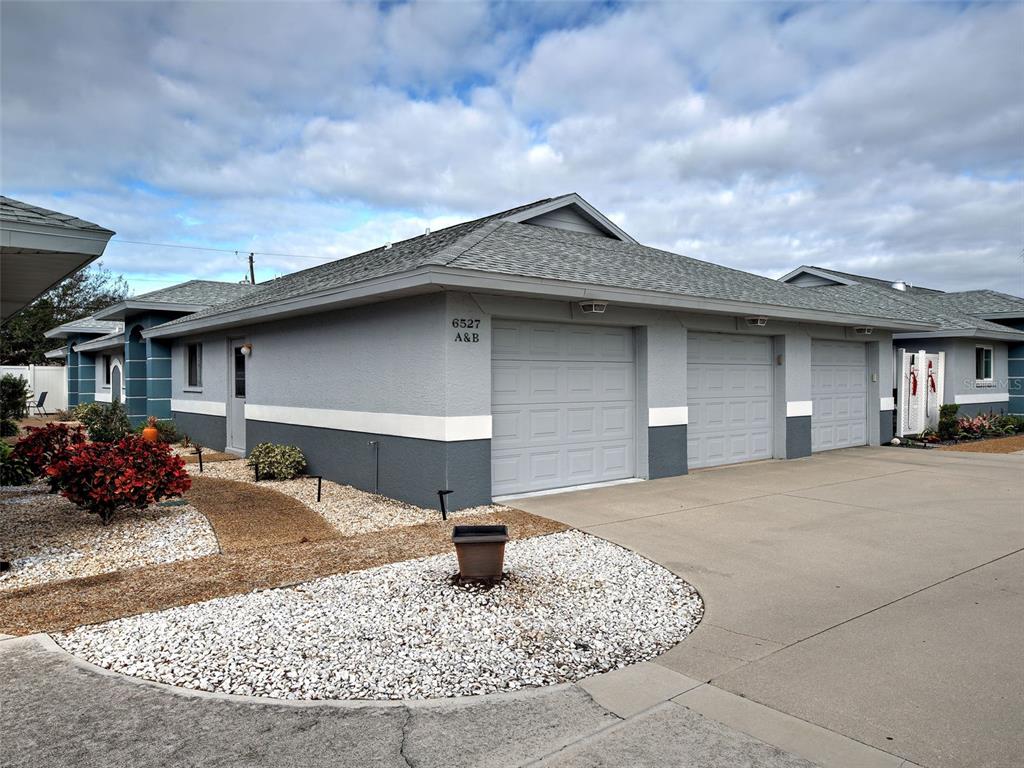 A gray duplex building features three garage doors and a gravel front yard — 6527 HAMLET DRIVE UNIT 26B, ENGLEWOOD, FL