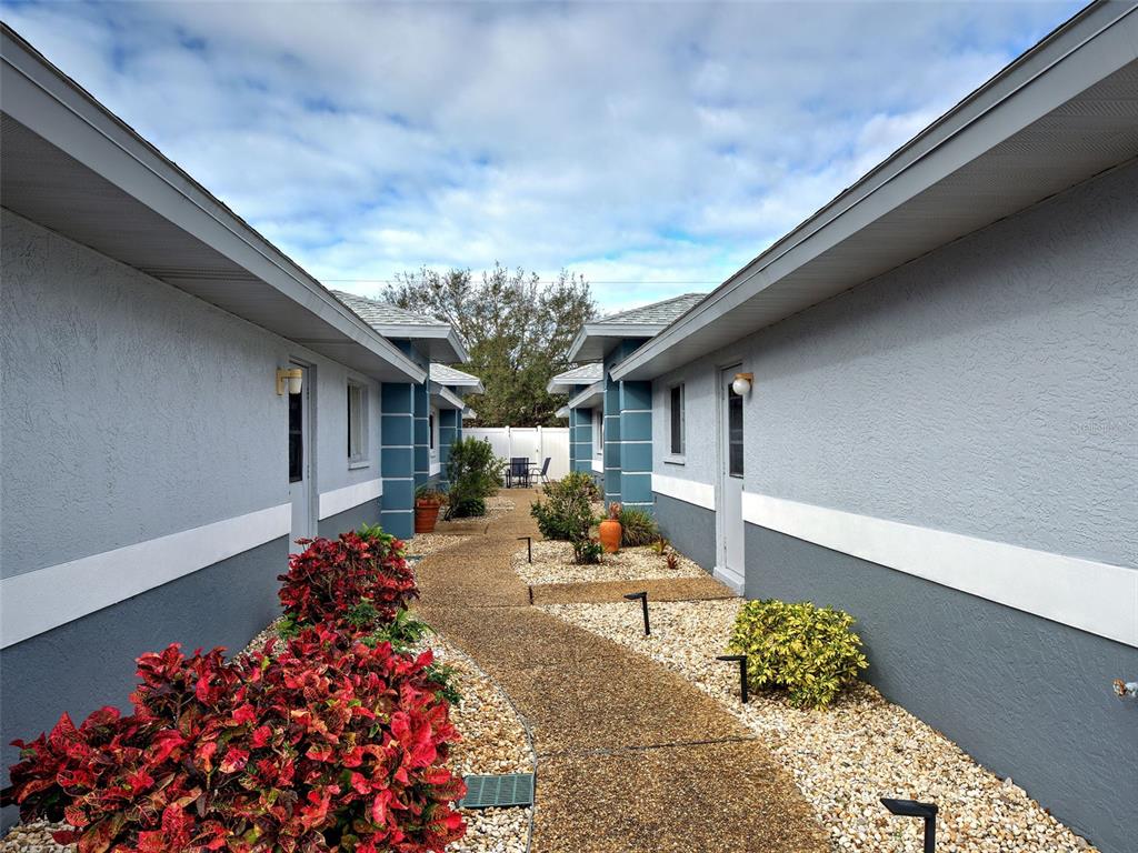 A paved walkway leads between two gray buildings with decorative landscaping and exterior lighting — 6527 HAMLET DRIVE UNIT 26B, ENGLEWOOD, FL