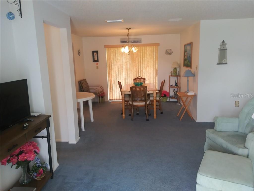 A dining area with a table and chairs sits beyond a carpeted living room — 1261 JOPLIN AVENUE NW, PORT CHARLOTTE, FL