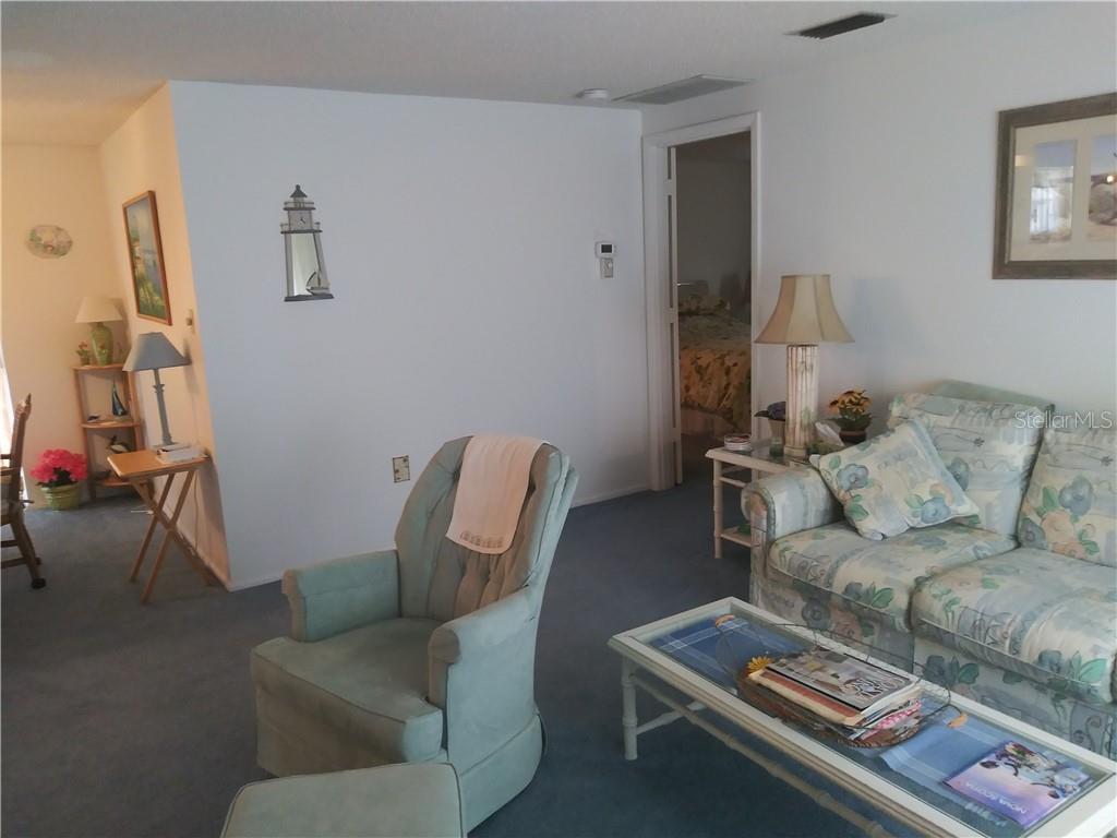 A living room features blue carpeting, a floral sofa, a matching armchair, and a coffee table — 1261 JOPLIN AVENUE NW, PORT CHARLOTTE, FL