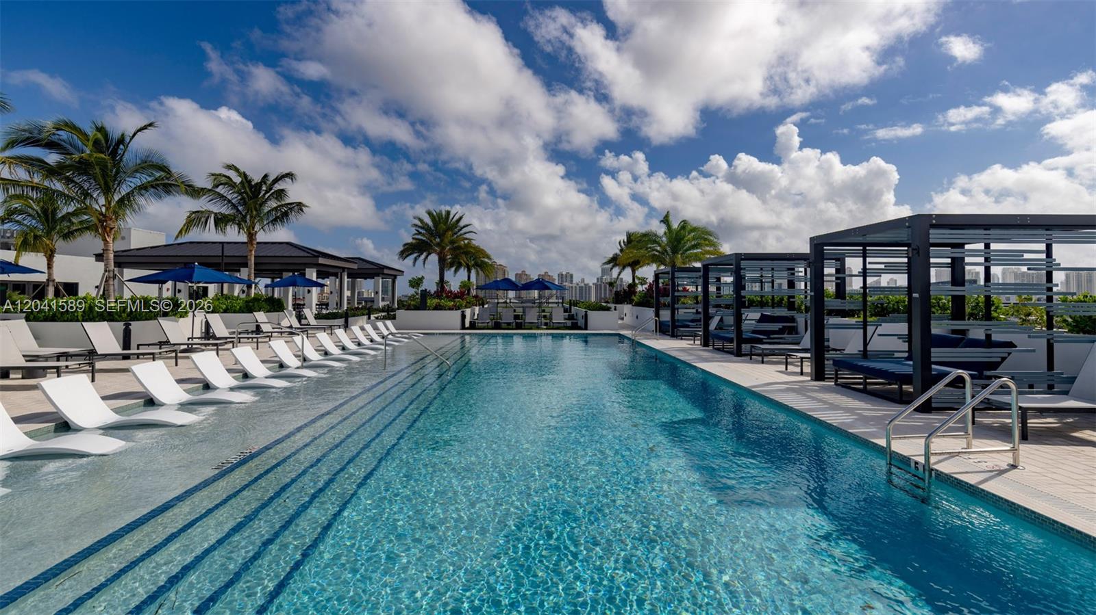 A rooftop swimming pool features lounge chairs, cabanas, and palm trees under a cloudy sky — 19401 W Dixie Hwy # 421, Miami FL 33180, MIAMI, FL