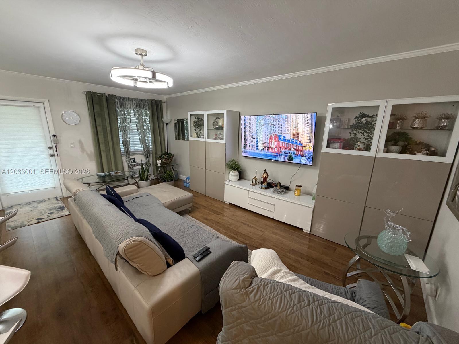 A living room features a sectional sofa, a wall-mounted television, and built-in storage cabinets — 500 Layne Blvd # 12, Hallandale Beach FL 33009, HALLANDALE BEACH, FL