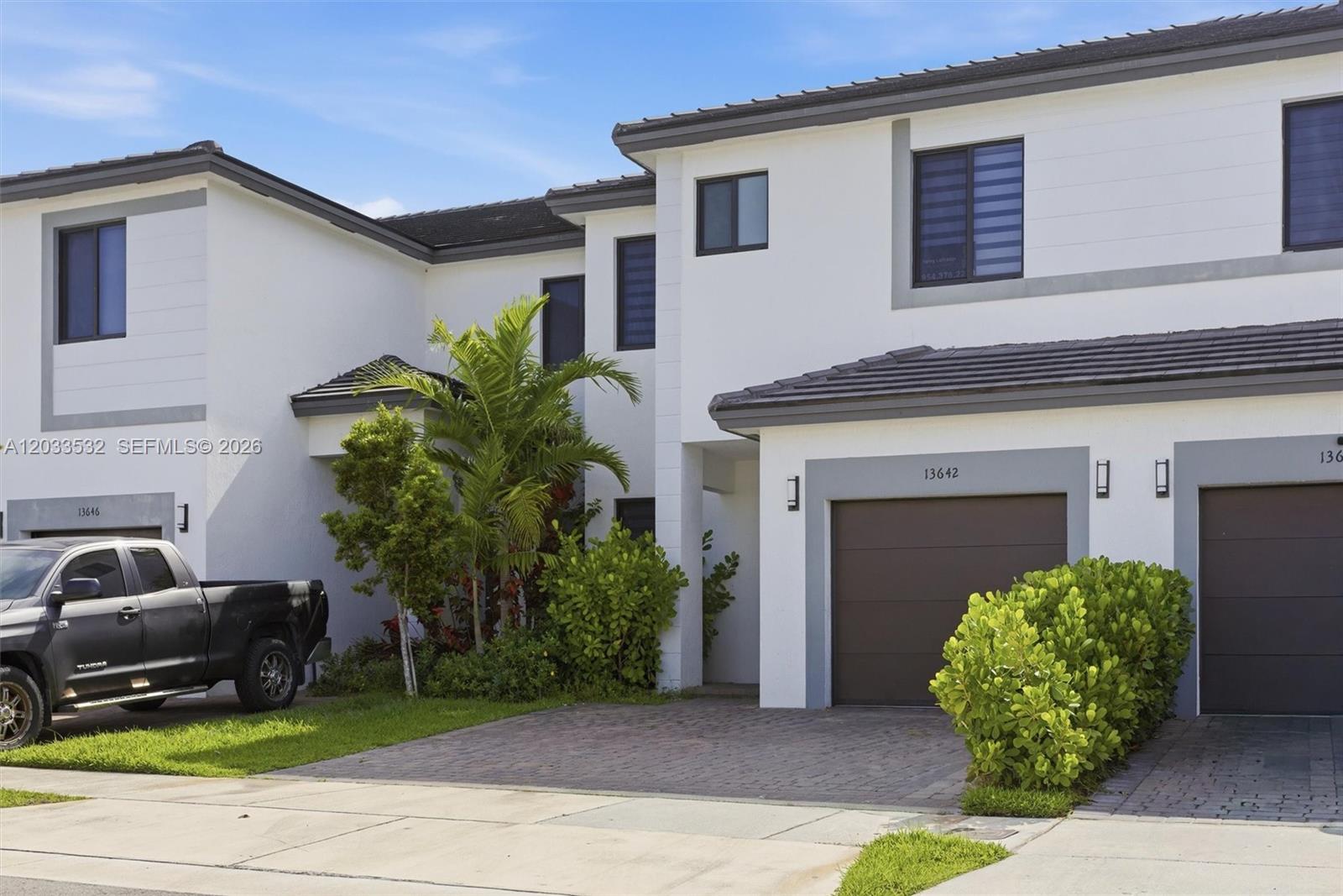 A two-story townhouse exterior features white stucco walls, dark-framed windows, and a paved driveway — 13642 SW 157th PL, Miami FL 33196, MIAMI, FL