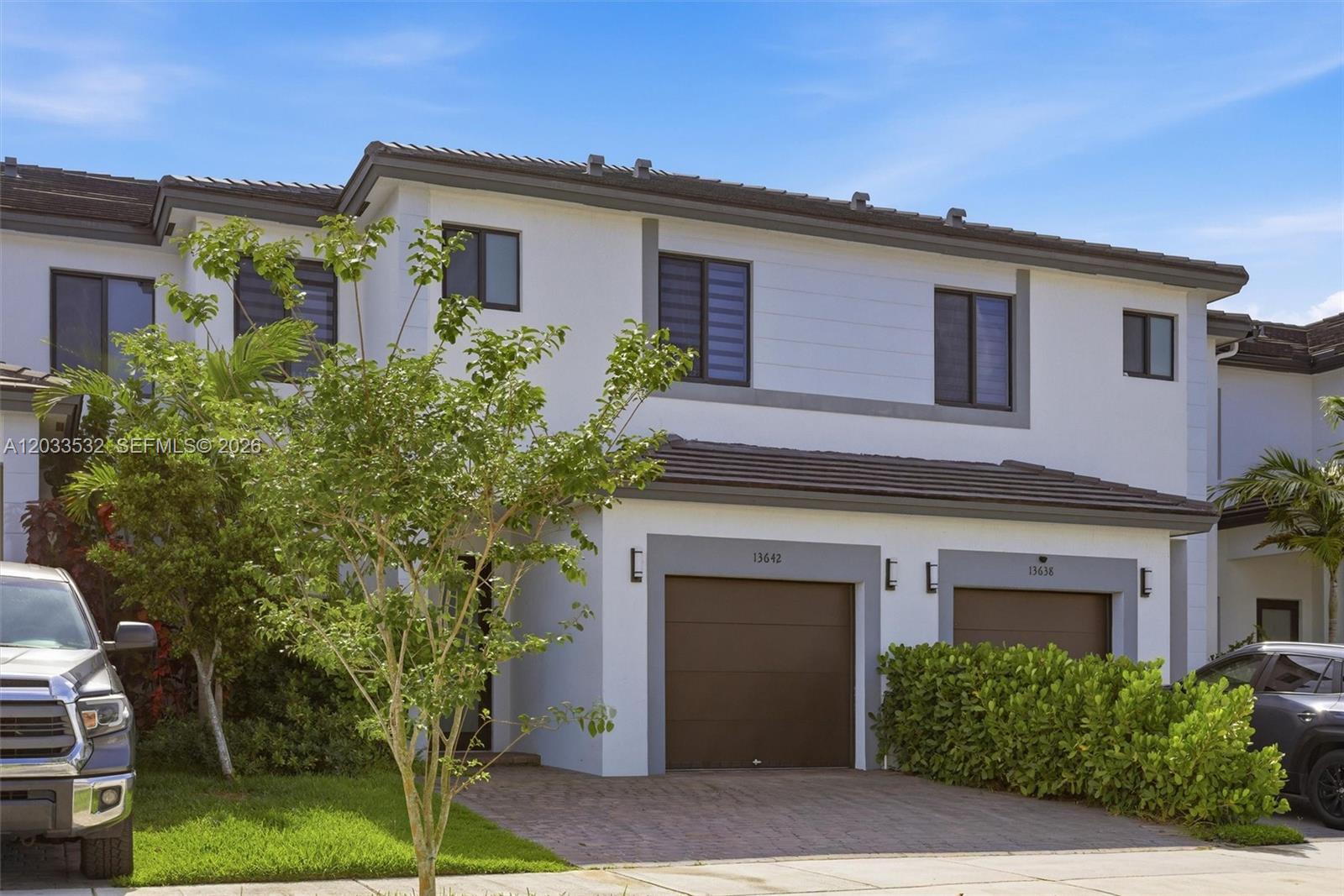 A two-story townhouse exterior features white stucco walls, brown garage doors, and a tiled roof — 13642 SW 157th PL, Miami FL 33196, MIAMI, FL