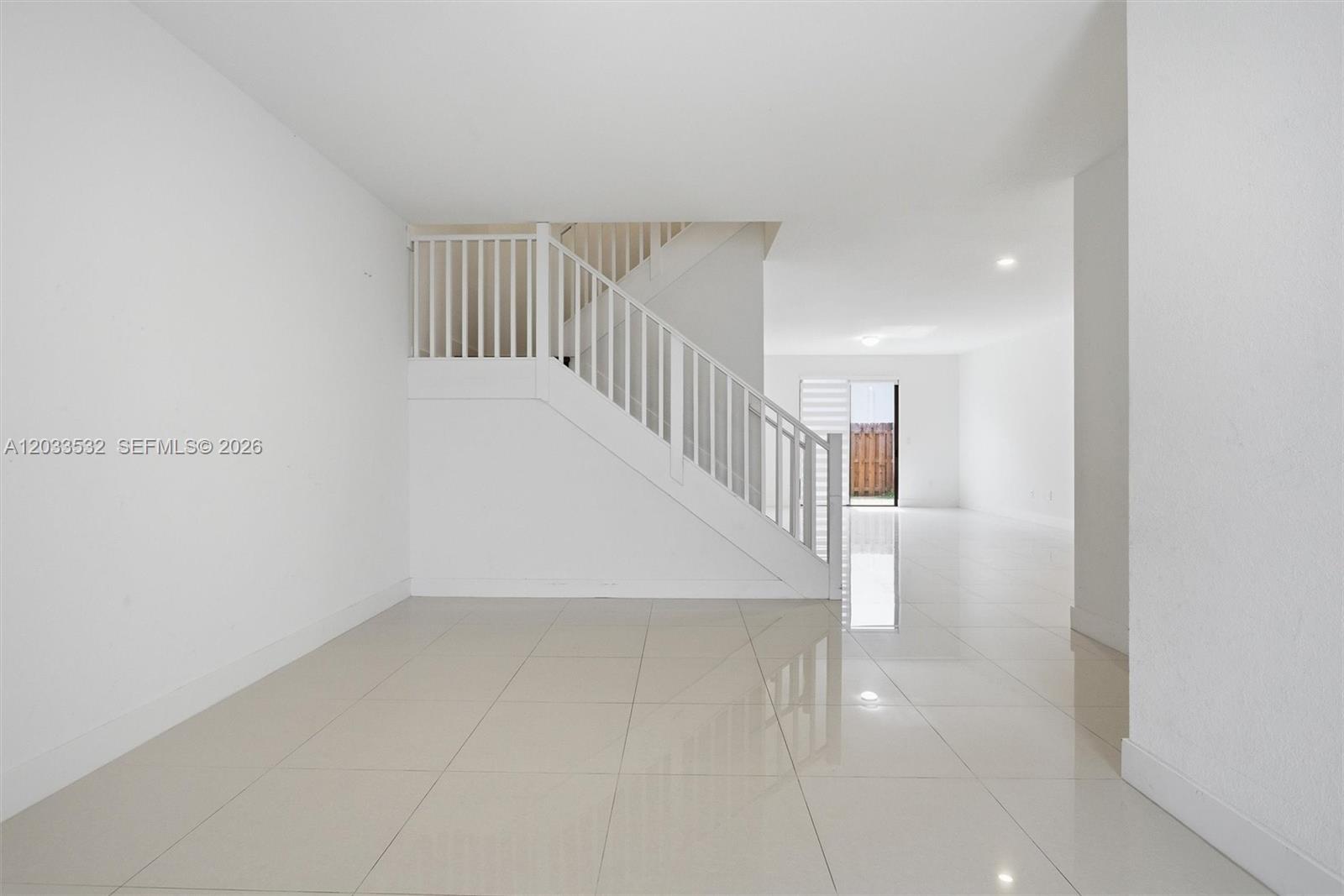 A bright, minimalist room features white walls, glossy tile floors, and a white staircase — 13642 SW 157th PL, Miami FL 33196, MIAMI, FL