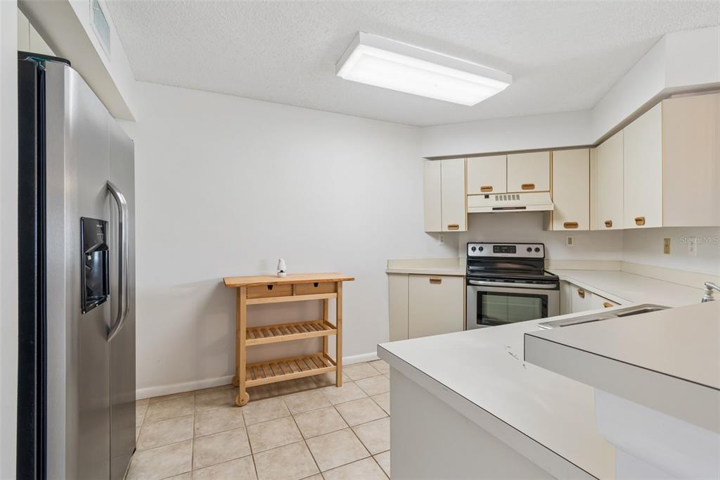 A kitchen featuring white cabinets, stainless steel appliances, tile flooring, and a wooden rolling cart — 6000 BAHIA DEL MAR CIRCLE UNIT 134, ST PETERSBURG, FL