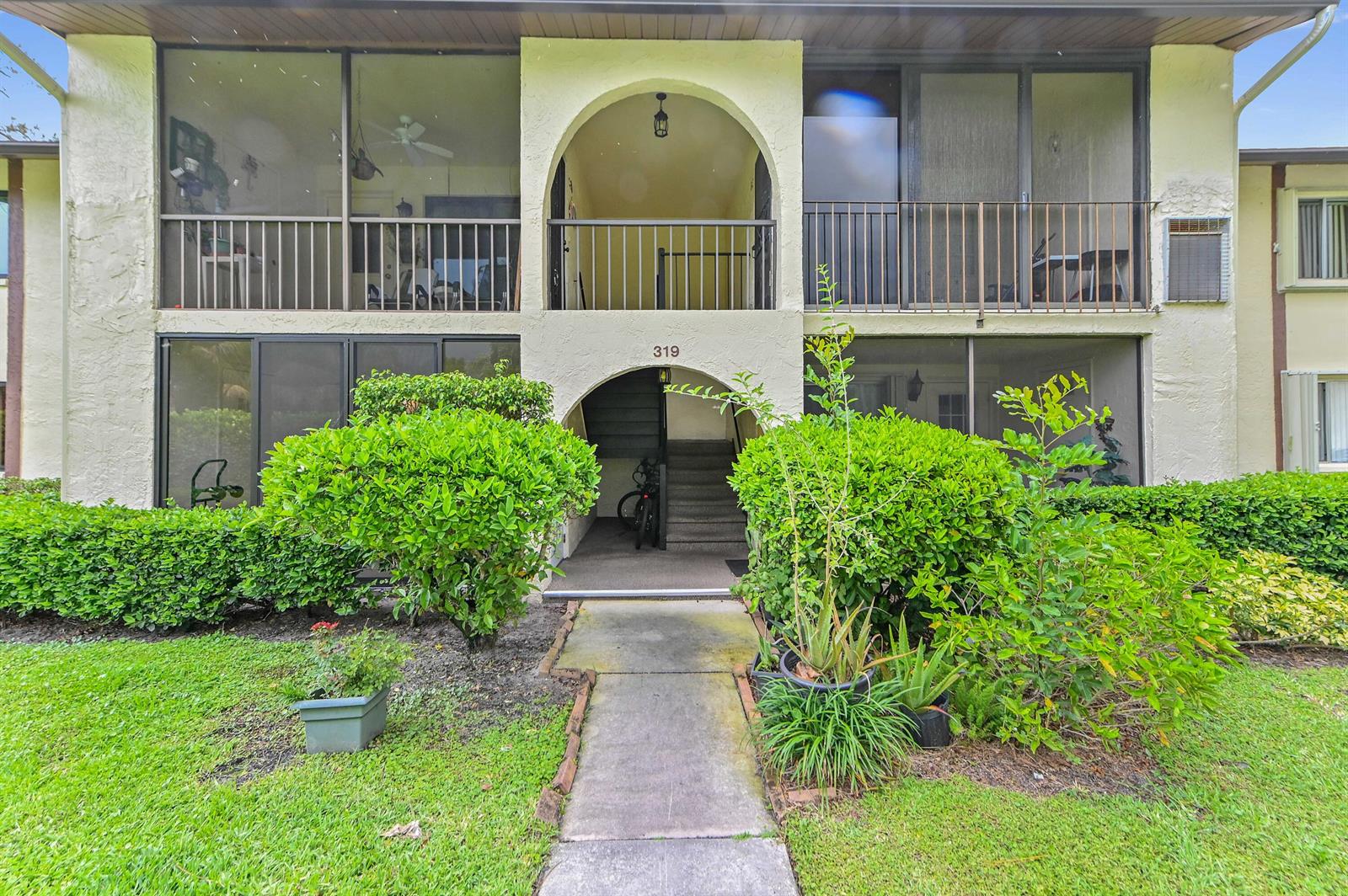 A two-story apartment building exterior features screened balconies, arched entryways, and a concrete walkway — 319 Knotty Pine Circle # 1, FL 33463, FL