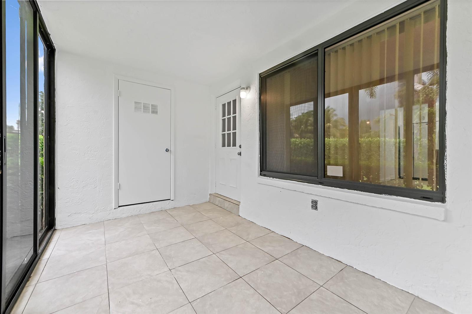 A covered patio features white walls, tiled flooring, a glass door, and a large window — 319 Knotty Pine Circle # 1, FL 33463, FL