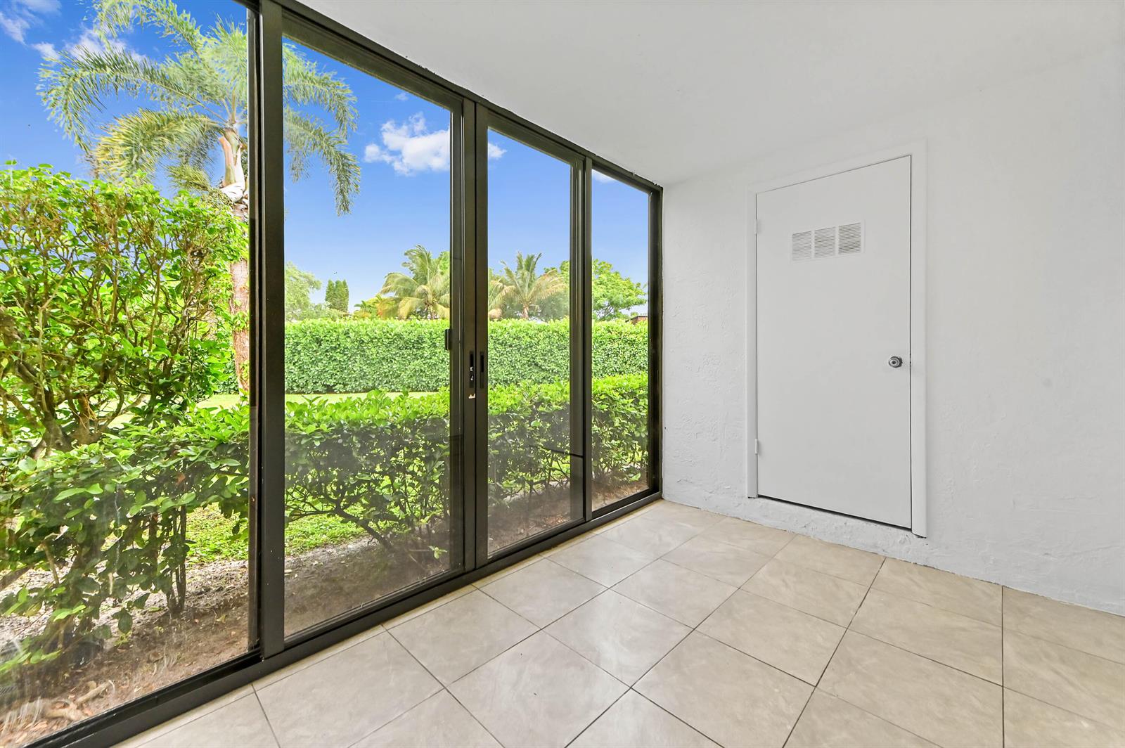 A sunroom with tile flooring, a white door, and large sliding glass doors overlooking greenery — 319 Knotty Pine Circle # 1, FL 33463, FL