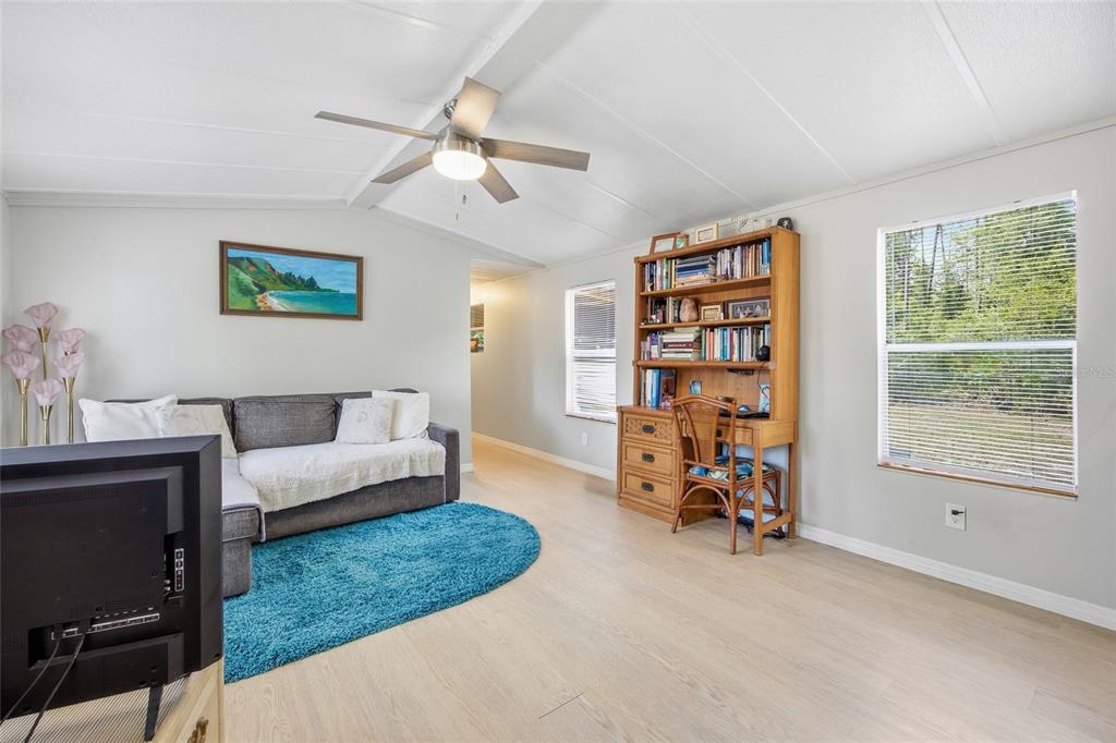 A living room features light wood-look flooring, a gray sectional sofa, and a wooden desk — 2412 NW 116TH PLACE, GAINESVILLE, FL