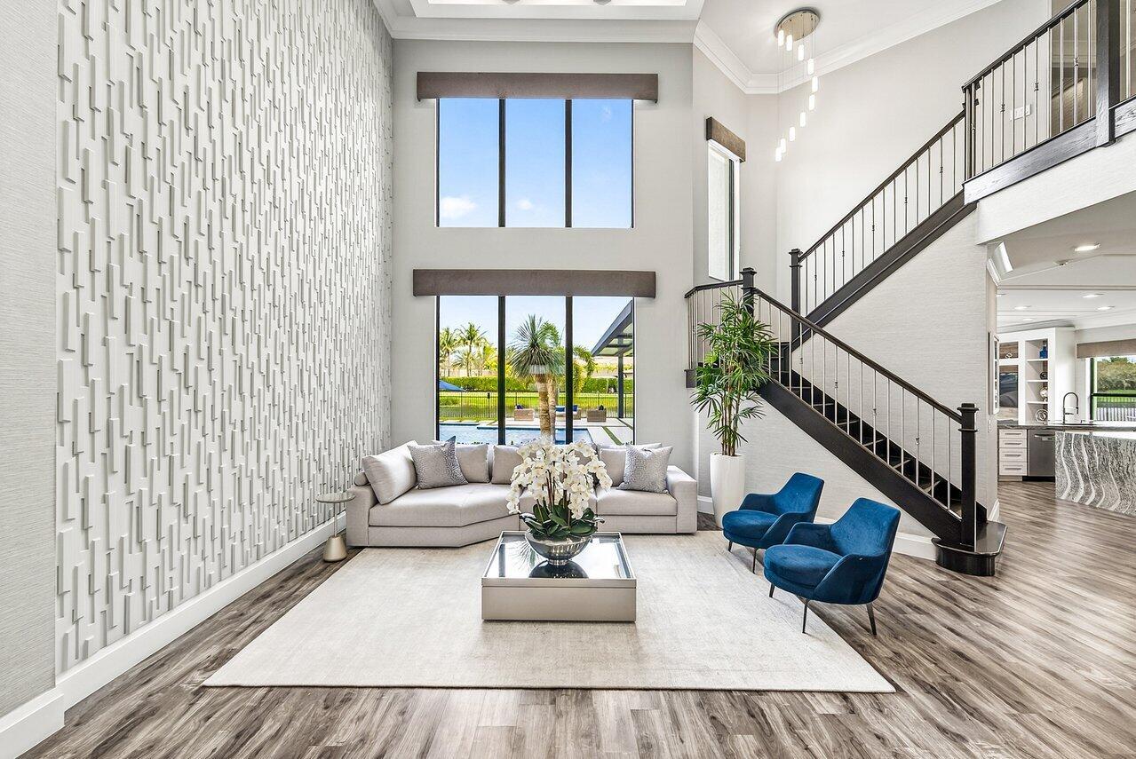 A modern living room features a textured accent wall, tall windows, and a staircase — 16722 Cannes Street, Delray Beach FL 33446, DELRAY BEACH, FL