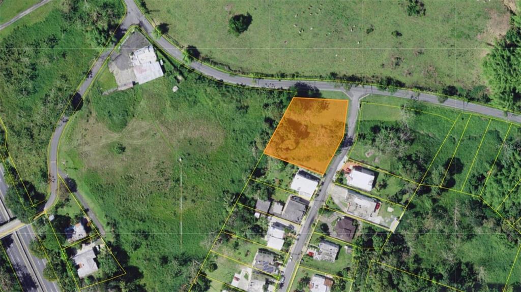 An aerial view shows an orange-highlighted vacant lot situated along a paved road — BO CEIBA SUR BRISAS DEL PEDREGAL SOLAR #1, JUNCOS, PR