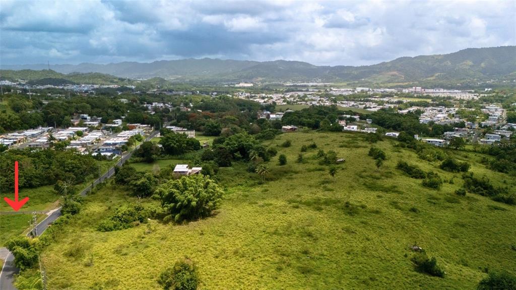 An aerial view shows a large, grassy, undeveloped plot of land next to a paved road — BO CEIBA SUR BRISAS DEL PEDREGAL SOLAR #1, JUNCOS, PR