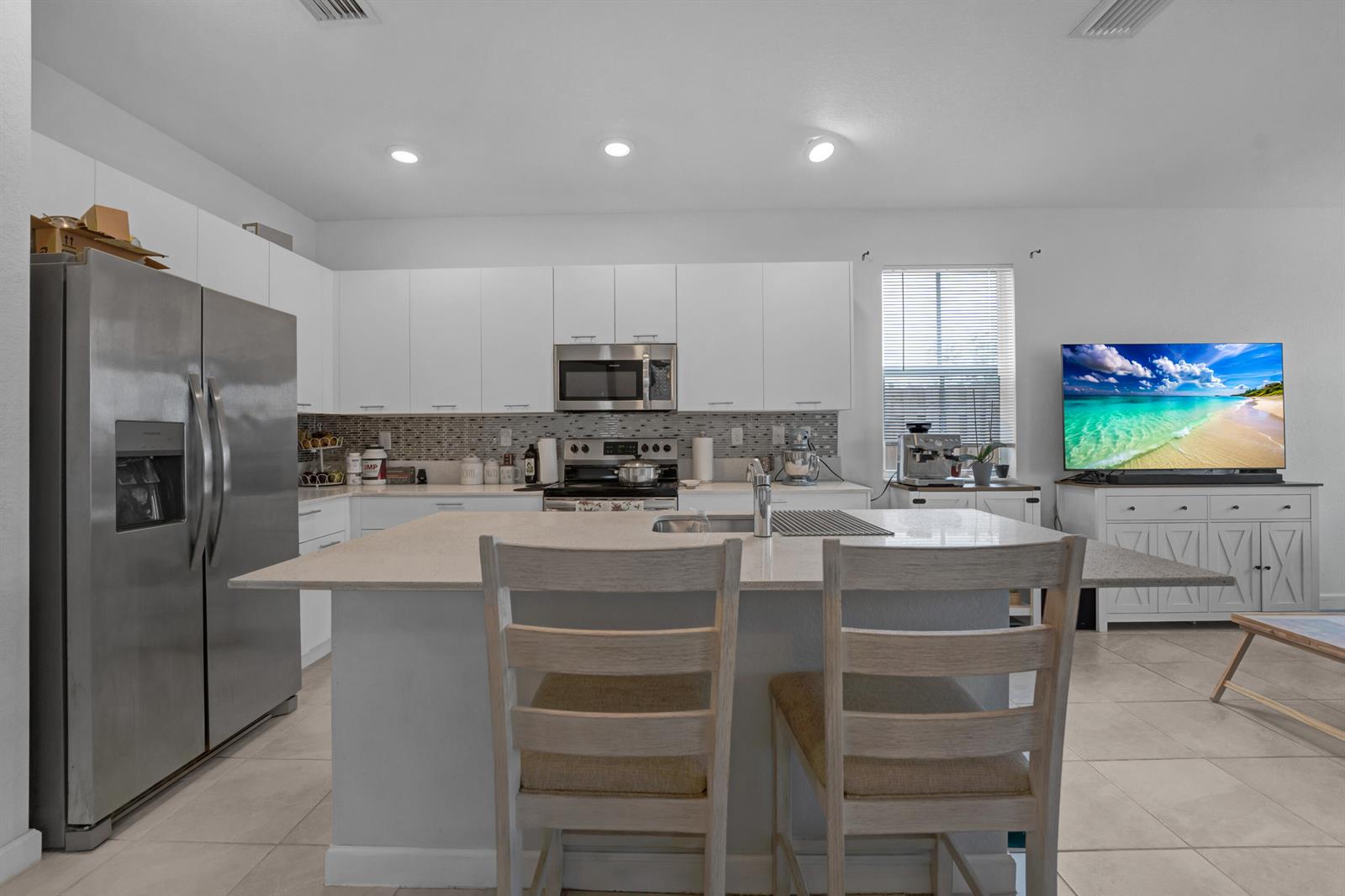 A modern kitchen features white cabinetry, stainless steel appliances, and a central island with seating — 2409 NW 131st Circle, Miami FL 33167, MIAMI, FL