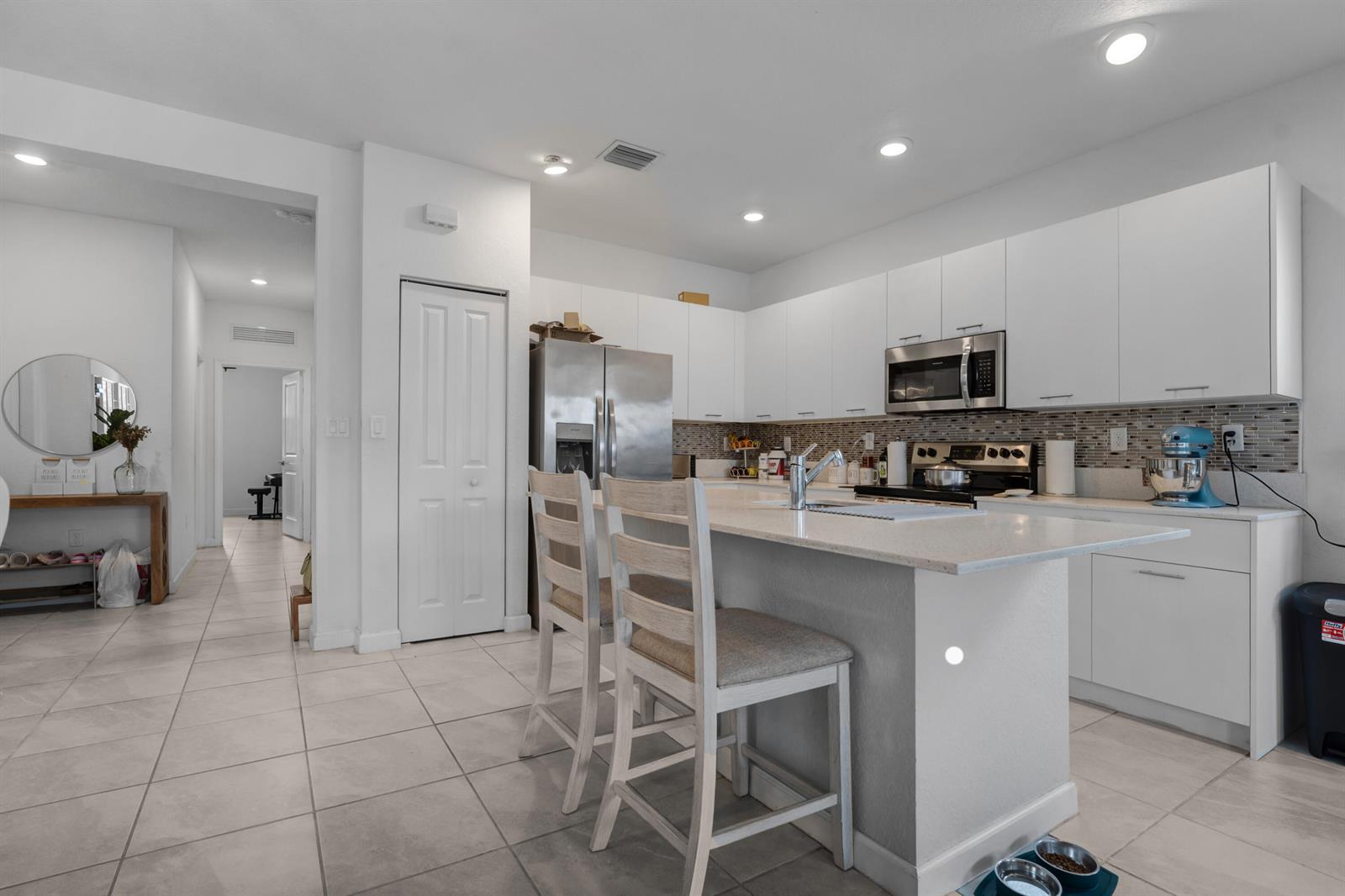 A modern kitchen features white cabinetry, stainless steel appliances, a quartz island, and tile flooring — 2409 NW 131st Circle, Miami FL 33167, MIAMI, FL