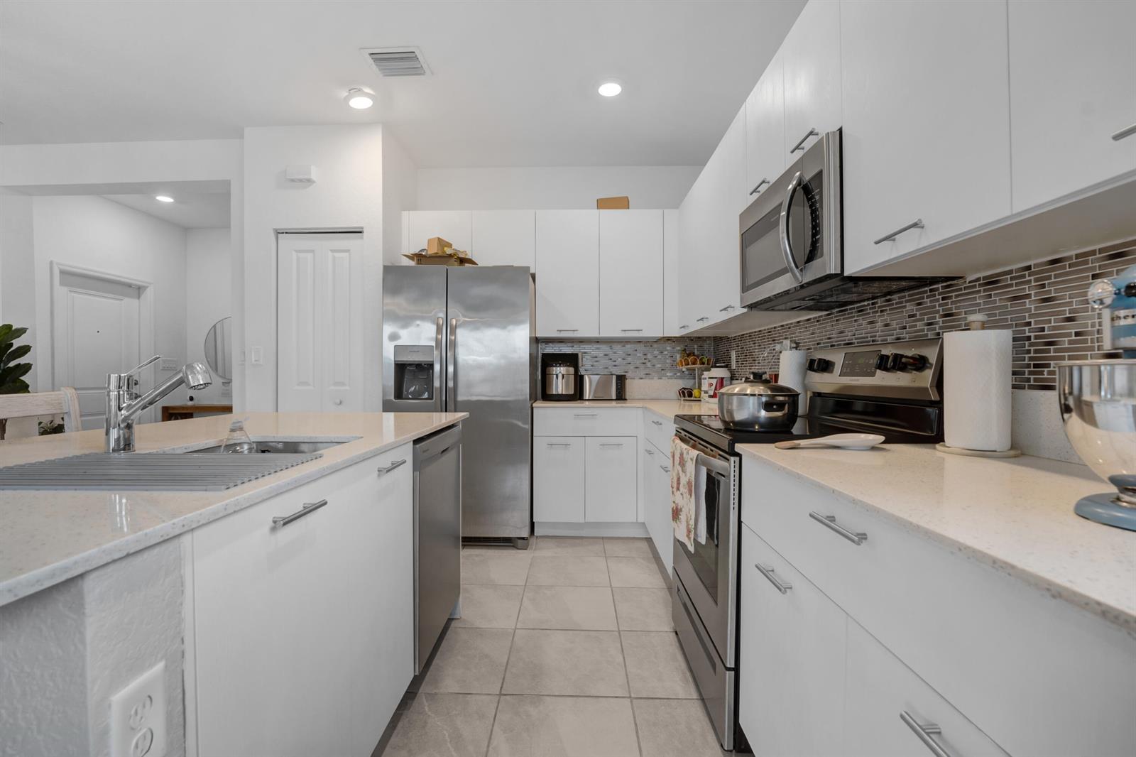 A modern kitchen features white cabinetry, stainless steel appliances, and a central island with sink — 2409 NW 131st Circle, Miami FL 33167, MIAMI, FL