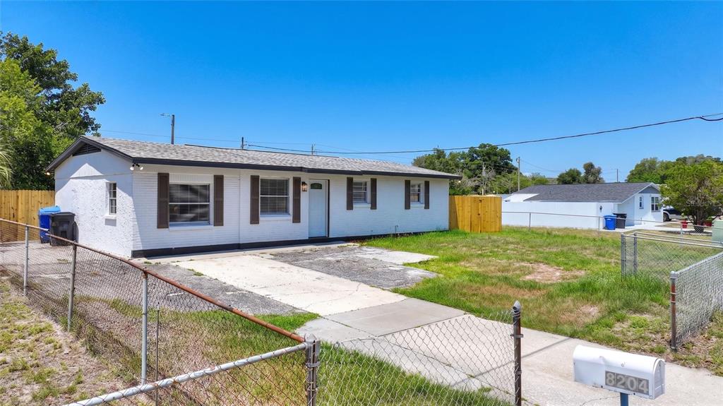 A white single-story house with a concrete driveway and chain-link fencing under a blue sky — 8204 ALLAMANDA AVENUE, TAMPA, FL