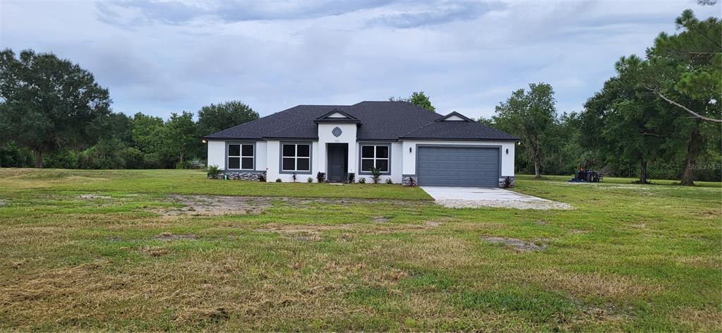 A single-story house with a gray garage, white exterior, and dark roof sits on grass — 1685 E OSCEOLA ROAD, GENEVA, FL