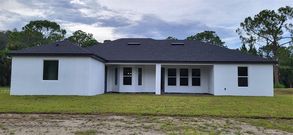The rear exterior of a white, single-story house features a dark shingled roof and windows — 1685 E OSCEOLA ROAD, GENEVA, FL