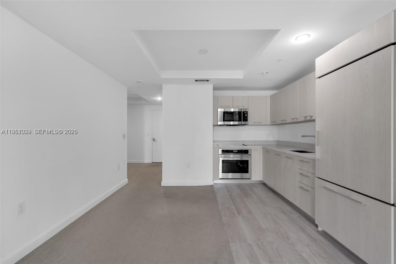 A kitchen with light wood cabinets and stainless steel appliances sits beside a carpeted area — 45 SW 9th St # 2204, Miami FL 33130, MIAMI, FL