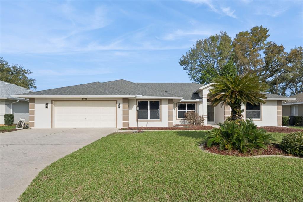 A single-story house with a white stucco exterior, a two-car garage, and a palm tree — 5729 KING JAMES AVENUE, LEESBURG, FL