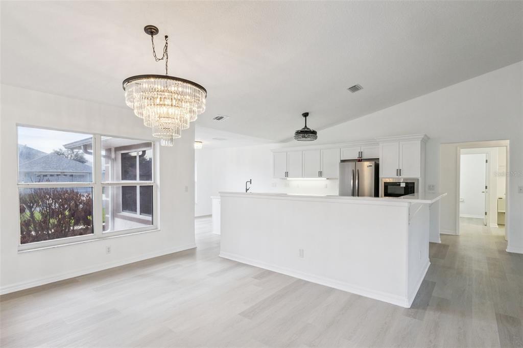 A bright kitchen and dining area features white cabinetry, a crystal chandelier, and light flooring — 5729 KING JAMES AVENUE, LEESBURG, FL