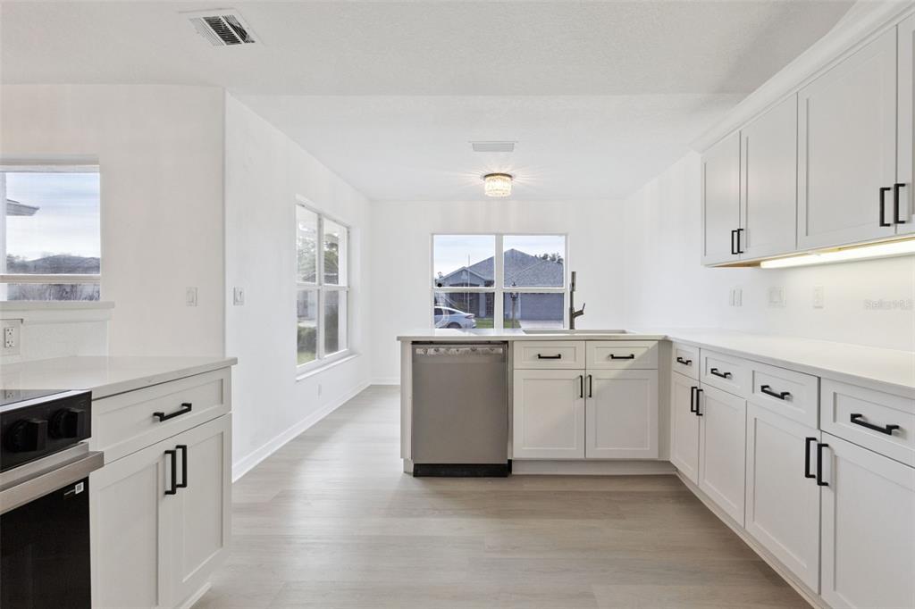A kitchen with white cabinets, stainless steel appliances, and light wood-look flooring — 5729 KING JAMES AVENUE, LEESBURG, FL