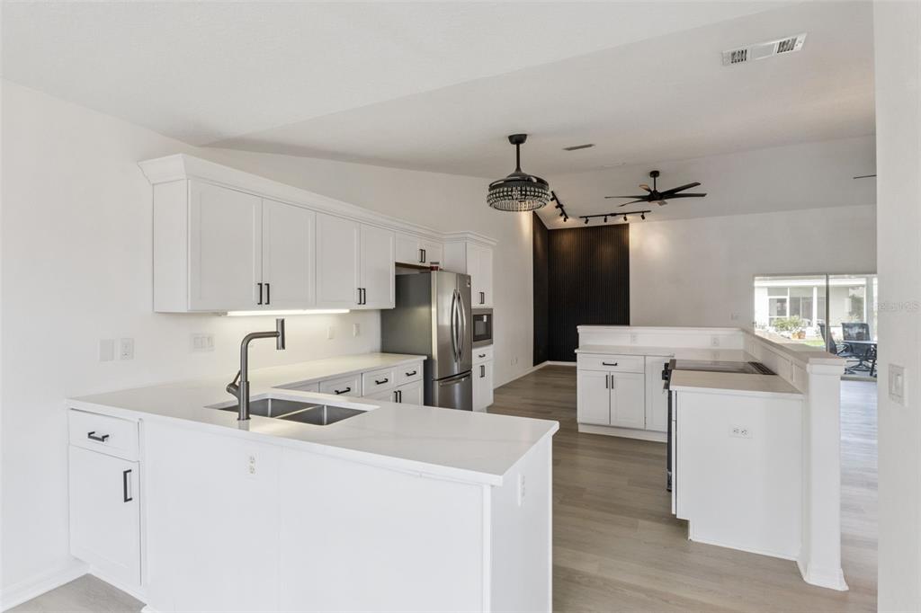 A bright kitchen features white cabinets, stainless steel appliances, and light wood-look flooring — 5729 KING JAMES AVENUE, LEESBURG, FL