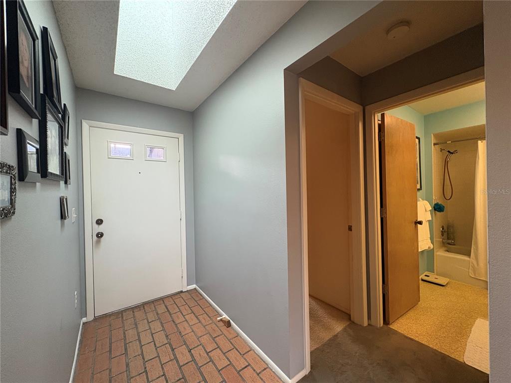 An entryway with brick flooring, a skylight, and a doorway leading to a bathroom — 7214 CLOISTER DRIVE UNIT 7214, SARASOTA, FL