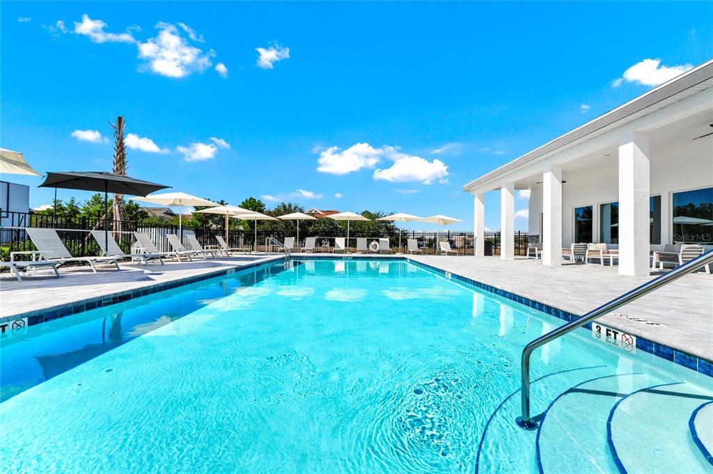 A swimming pool with lounge chairs and umbrellas sits beside a building with white columns — 637 TRIKOMO DRIVE DRIVE, DAVENPORT, FL