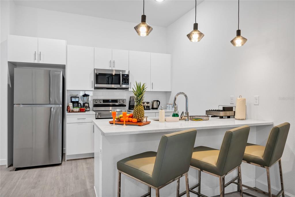 A modern kitchen features white cabinetry, stainless steel appliances, and a breakfast bar with stools — 637 TRIKOMO DRIVE DRIVE, DAVENPORT, FL