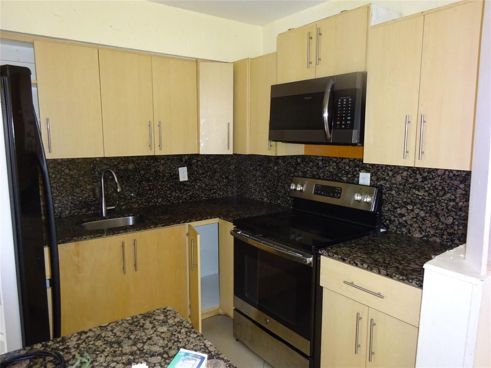 A kitchen features light wood cabinets, dark granite countertops, and stainless steel appliances — 740 E Evanston Circle E, Fort Lauderdale FL 33312, FORT LAUDERDALE, FL