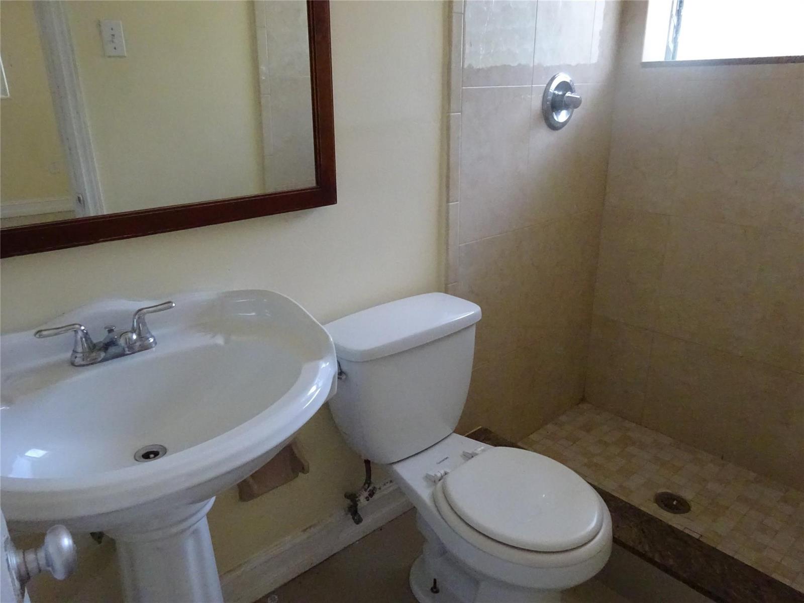 A bathroom features a pedestal sink, a white toilet, and a tiled walk-in shower — 740 E Evanston Circle E, Fort Lauderdale FL 33312, FORT LAUDERDALE, FL