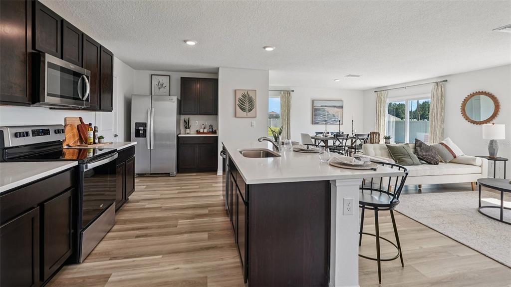 An open-concept kitchen with dark cabinets, stainless steel appliances, and an island overlooks the living area — 9091 SW 47TH COURT, OCALA, FL