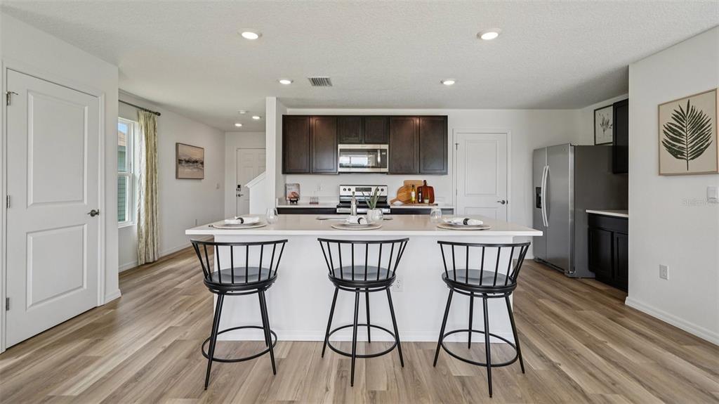 A kitchen features a white island with three black stools, dark cabinets, and wood-look flooring — 9091 SW 47TH COURT, OCALA, FL