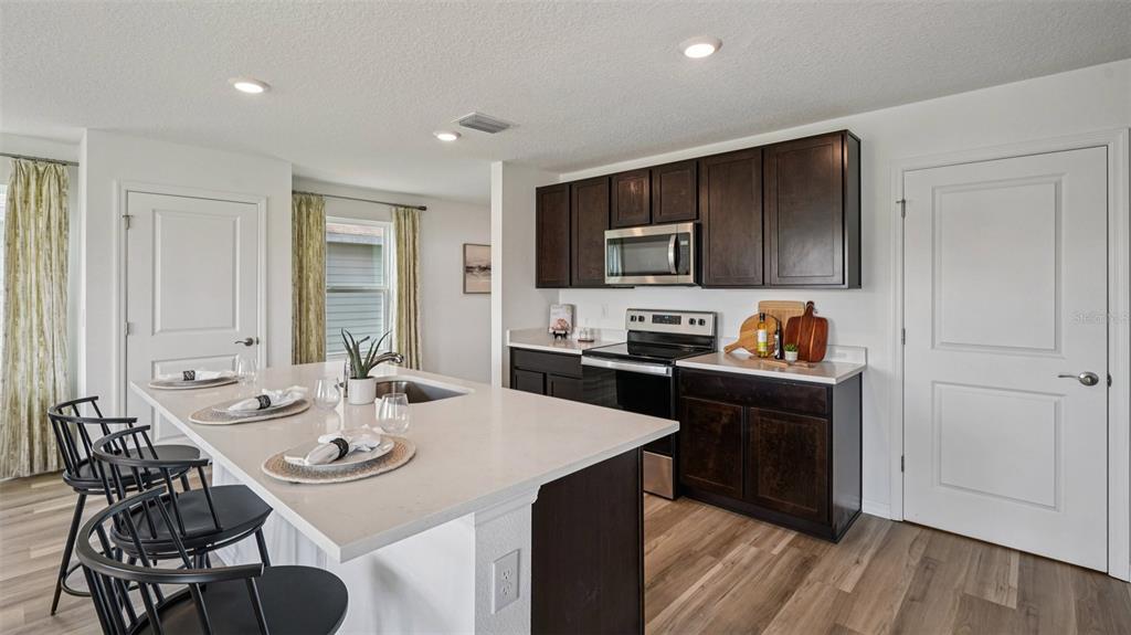 A kitchen features dark wood cabinets, a white quartz island with seating, and light flooring — 9091 SW 47TH COURT, OCALA, FL