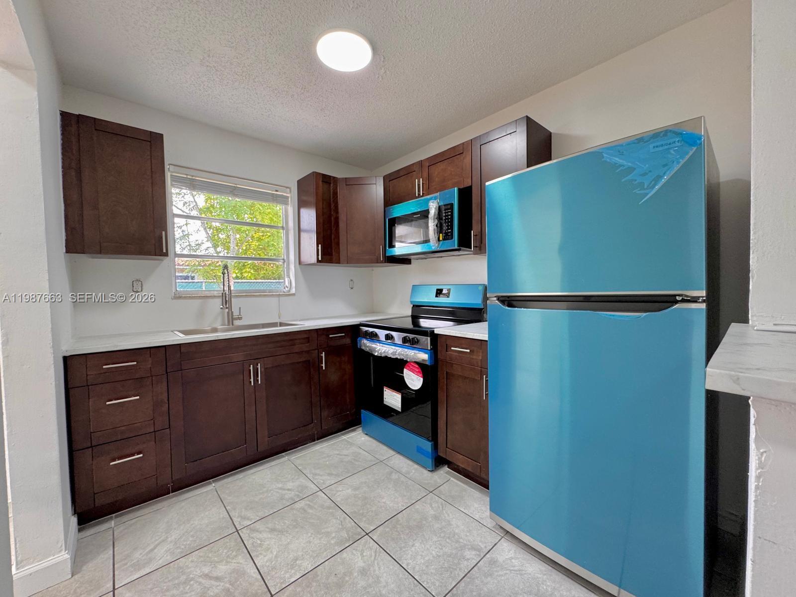 A kitchen features dark wood cabinets, stainless steel appliances, and light gray tiled flooring — 3630 SW 87th Ave, Miami FL 33165, MIAMI, FL