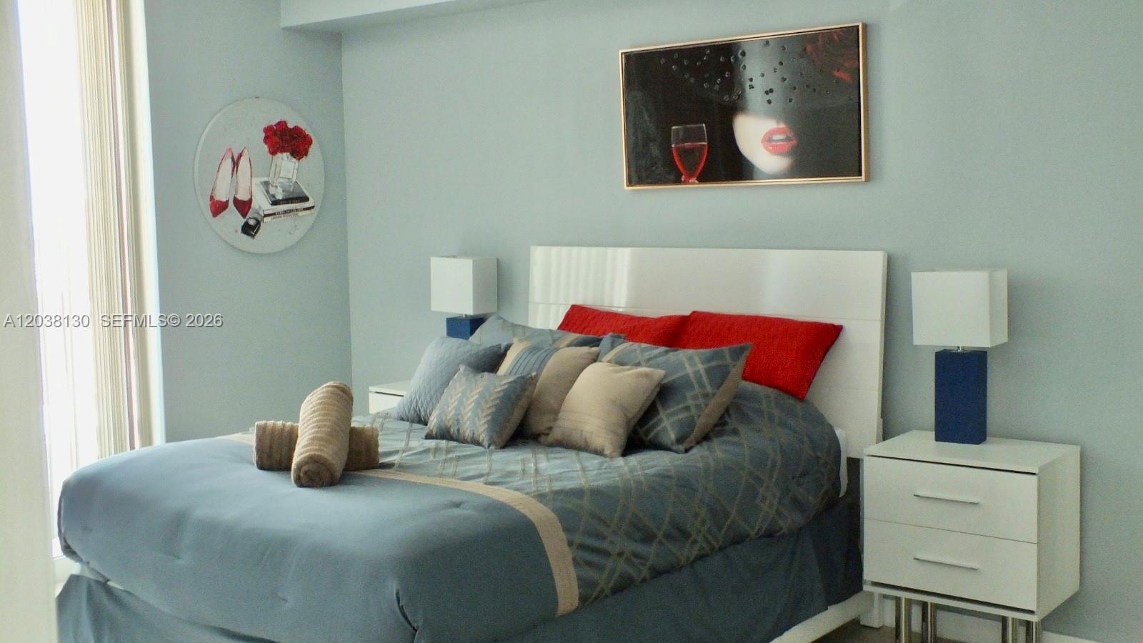 A bedroom features a bed with blue and red bedding, two nightstands, and wall art — 1200 Brickell Bay Dr # 4306, Miami FL 33131, MIAMI, FL