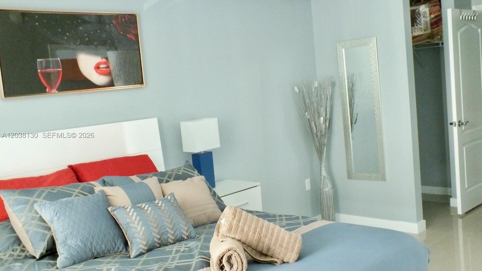 A bedroom features a bed with blue patterned bedding, a wall mirror, and framed artwork — 1200 Brickell Bay Dr # 4306, Miami FL 33131, MIAMI, FL