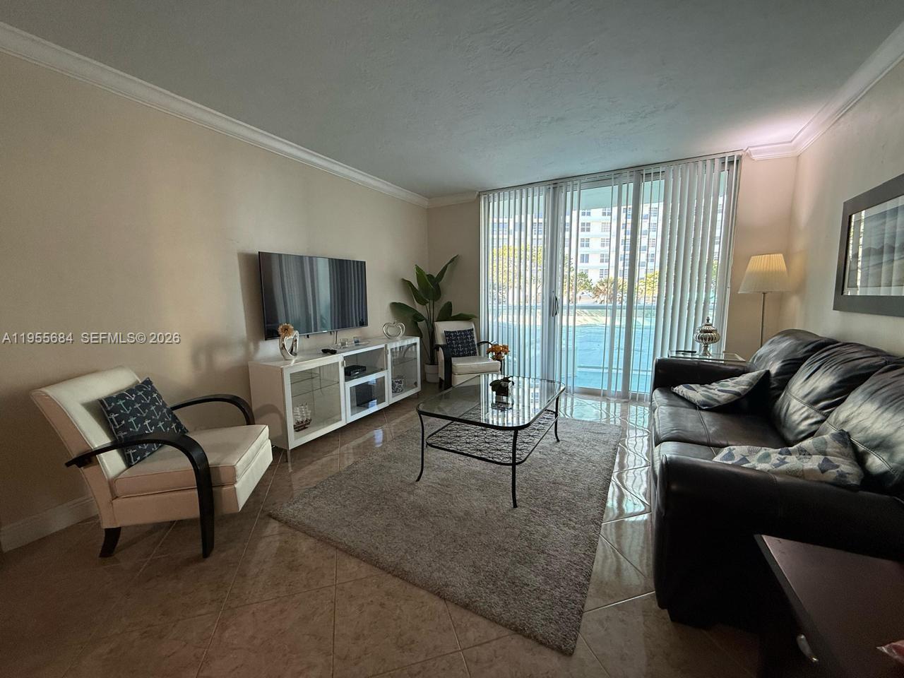 A living room features a dark leather sofa, a white media console, and tile flooring — 3801 S Ocean Dr # 2C, Hollywood FL 33019, HOLLYWOOD, FL