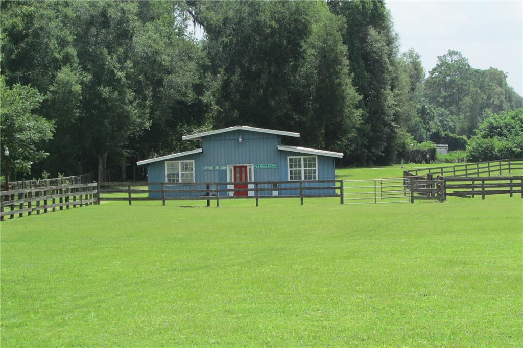 A blue barn-style building with a red door sits in a grassy, fenced pasture — 10455 NW GAINESVILLE ROAD, OCALA, FL