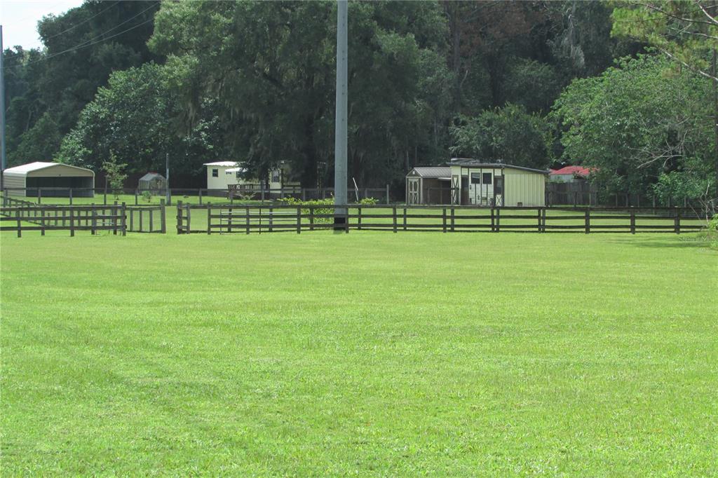 A large grassy field features a wooden fence and several small outbuildings in the background — 10455 NW GAINESVILLE ROAD, OCALA, FL