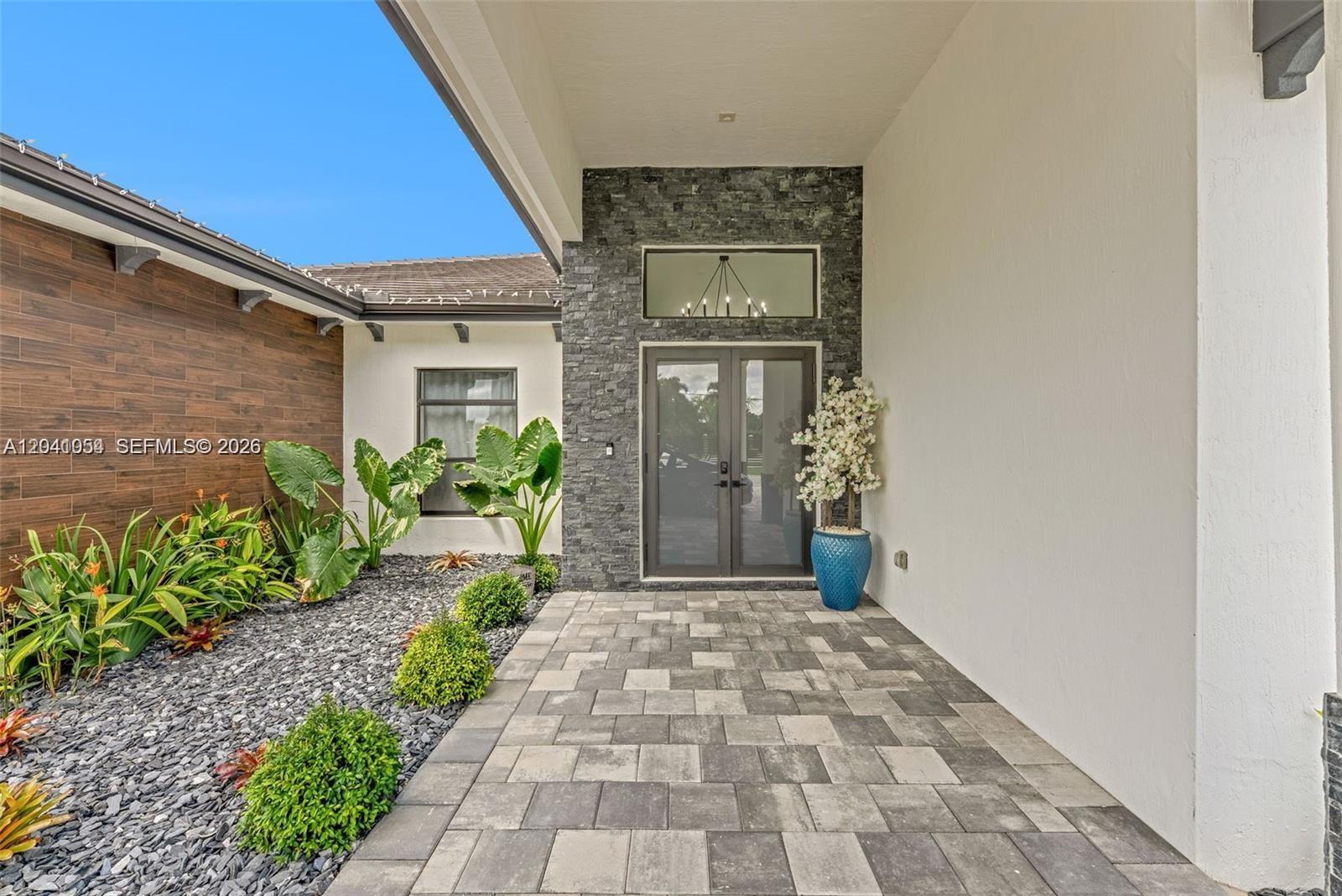 A modern home entrance features a stone facade, double glass doors, and a paved walkway — 18261 SW 224th St, Miami FL 33170, MIAMI, FL