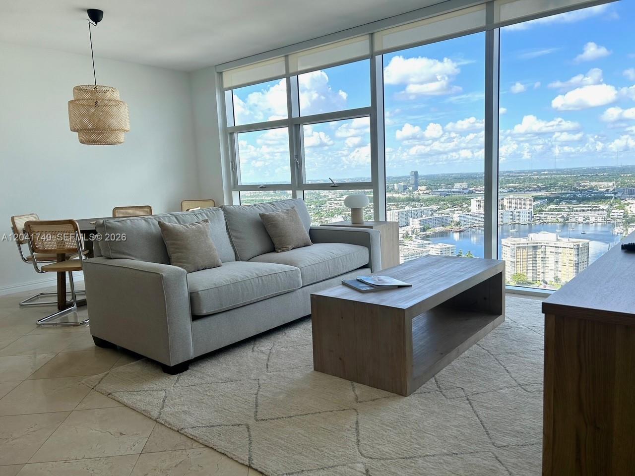 A living room features a gray sofa, a wooden coffee table, and floor-to-ceiling windows — 1830 S Ocean Dr # 3707, Hallandale Beach FL 33009, HALLANDALE BEACH, FL