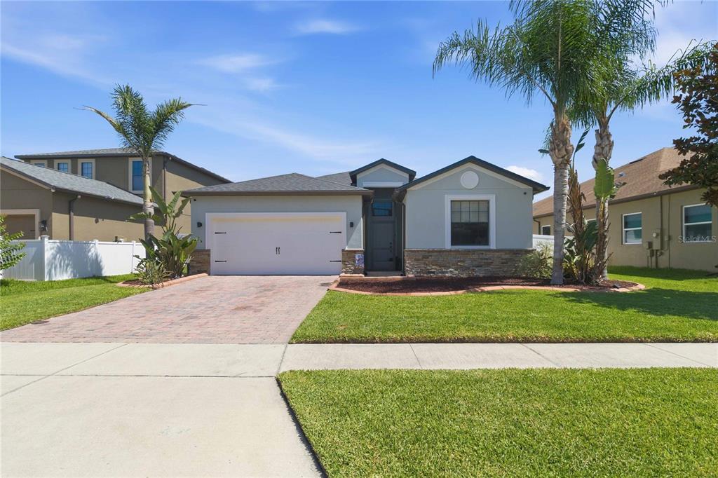 A single-story suburban house features a two-car garage, stone accents, and a paved driveway — 4355 SUMMER BREEZE WAY, KISSIMMEE, FL