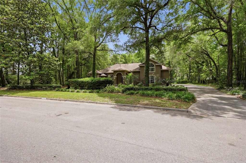 A two-story house with a brown exterior sits behind a lawn and mature trees — 4208 SW 96TH DRIVE, GAINESVILLE, FL