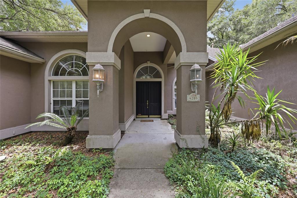 The exterior of a house features a covered entryway with double doors and arched windows — 4208 SW 96TH DRIVE, GAINESVILLE, FL
