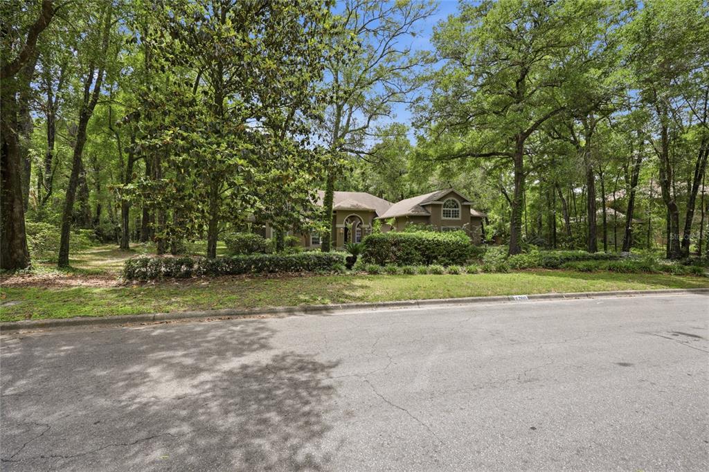 A single-story house with a brown exterior sits behind trees and a manicured hedge — 4208 SW 96TH DRIVE, GAINESVILLE, FL
