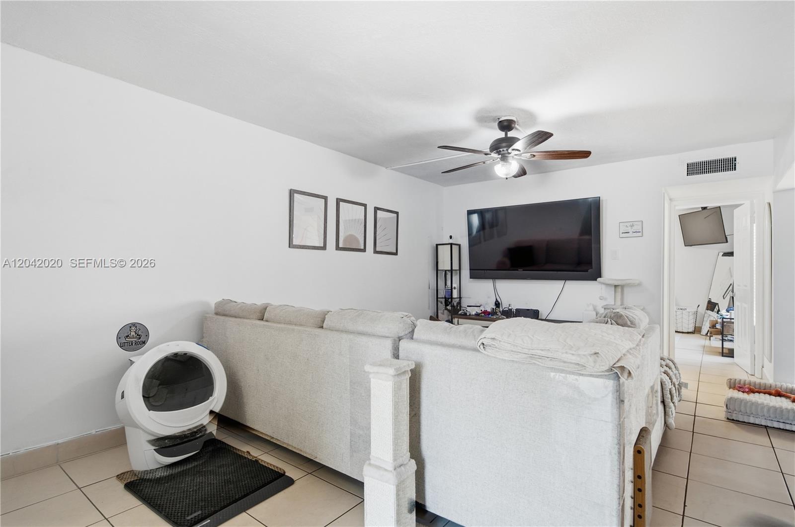 A living room features a large sectional sofa, a wall-mounted television, and a cat litter box — 10327 NW 9th St Cir # 7, Miami FL 33172, MIAMI, FL